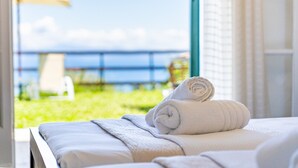 A bed with a rolled towel, a view of a grassy area, and a body of water. - Room 'Garden View 2' with Private Terrace, Wi-Fi and Air Conditioning (Corfu)
