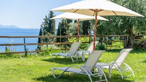 Outdoor seating with umbrellas, a wooden fence, and a view of the water. - Room 'Garden View 2' with Private Terrace, Wi-Fi and Air Conditioning (Corfu)