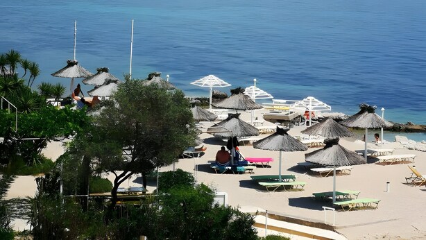 A beach with thatched umbrellas and lounge chairs, a clear view of the sea, and a hilly landscape in the background. - Room 'Two Bedroom' with Private Terrace, Wi-Fi and Air Conditioning (Corfu)
