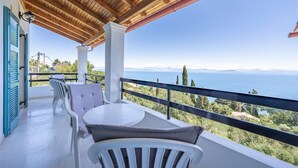 A balcony with a wooden ceiling, white chairs, a table, and a view of the sea and mountains. - Room 'Two Bedroom' with Private Terrace, Wi-Fi and Air Conditioning (Corfu)