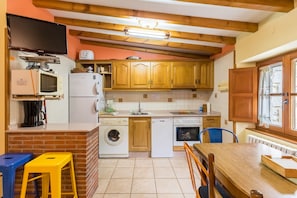 A compact kitchen with wooden cabinets, a washing machine, a dishwasher, a microwave, and a TV mounted on the wall.