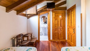 Una habitación con vigas de madera, una cama, un escritorio, una silla y un televisor.
