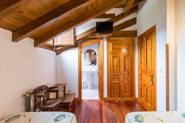 A room with wooden beams, a bed, a desk, a chair, and a television.