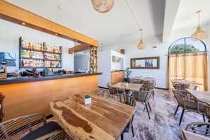 Eine Bar mit einer Holztheke, Korbmöbeln und einer Auswahl an Flaschen in Regalen.