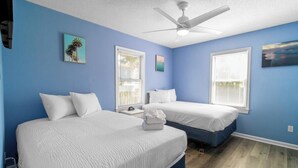 A bedroom with two beds, a ceiling fan, and artwork on the walls.