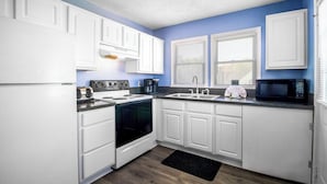 A compact kitchen with white cabinets, a stove, a sink, and a microwave.