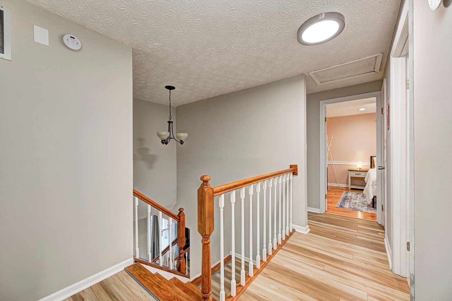 Un couloir avec un escalier en bois, un luminaire au plafond et une porte donnant sur une autre pièce.