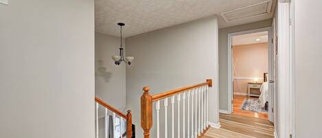 Un couloir avec un escalier en bois, un luminaire au plafond et une porte donnant sur une autre pièce.
