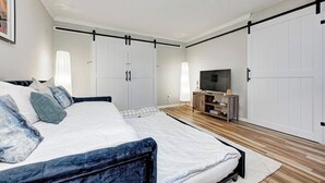A bedroom with a bed, wardrobe, TV stand, and a large wardrobe with sliding doors.