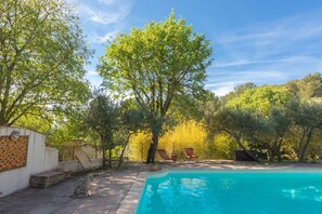 Una piscina con sillas de descanso, una estatua de piedra y árboles al fondo.
