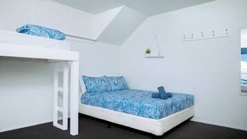Un dormitorio con una litera, una cama individual con ropa de cama estampada, una planta pequeña en un estante y una lámpara en el techo.