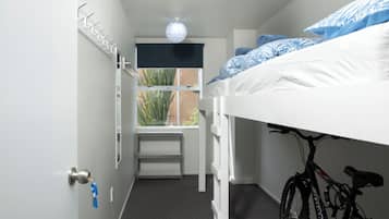 A bunk bed room with a bicycle, a window with a view of plants, and a door with a key.