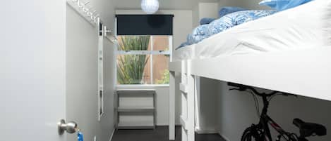 A bunk bed room with a bicycle, a window with a view of plants, and a door with a key.