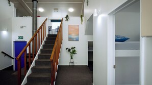 A hotel hallway with a staircase, a blue exit door, a plant, and a painting on the wall. - The Boathouse Lodge (Picton)