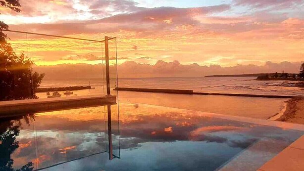 Una piscina con fondo de cristal que refleja la puesta de sol sobre el océano.