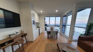 Una sala de estar moderna con televisor de pantalla plana, muebles de madera, zona de comedor y balcón con vistas al mar.
