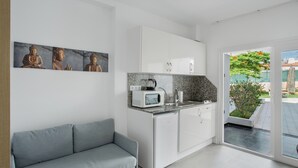 Una cocina moderna con armarios blancos, un microondas y un fregadero. Hay un sofá gris y una ventana con vistas a zonas verdes.