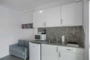Une cuisine compacte avec des meubles blancs, un plan de travail en granit, un petit réfrigérateur, un four à micro-ondes, une bouilloire et un évier.