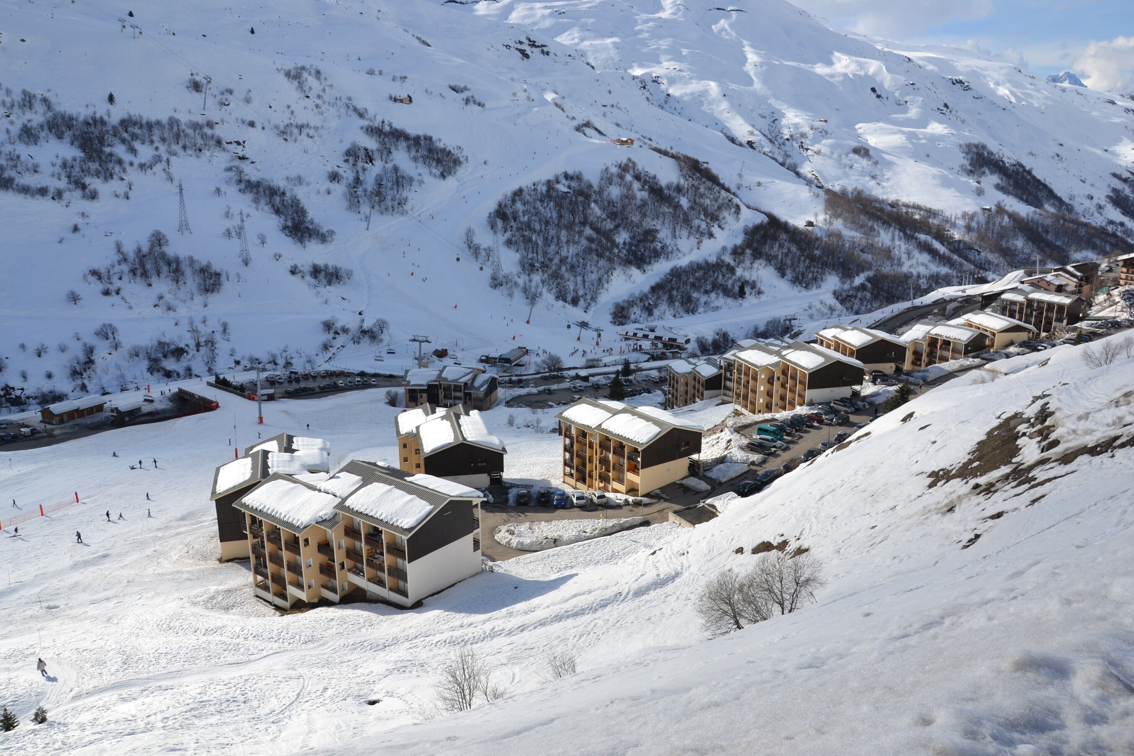 A snow-covered mountain resort with chalet-style buildings, ski slopes, and a clear view of the surrounding mountains.