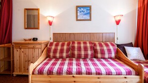 Una cama de madera con ropa de cama escocesa, una mesita de noche de madera, un espejo y dos lámparas fijadas a la pared.