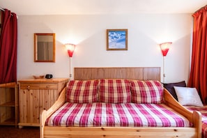 Un letto di legno con biancheria a quadri, un comodino di legno, uno specchio e due lampade fissate al muro.