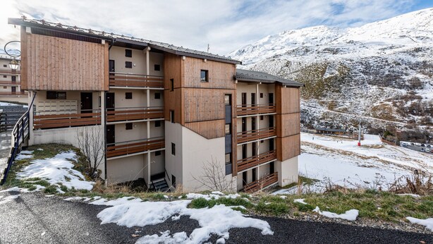 Un edificio de varios pisos con fachada de madera, balcones y vistas a montañas nevadas.