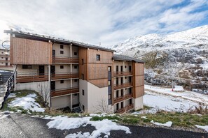 Un edificio a più piani con facciata in legno, balconi e vista sulle montagne innevate.