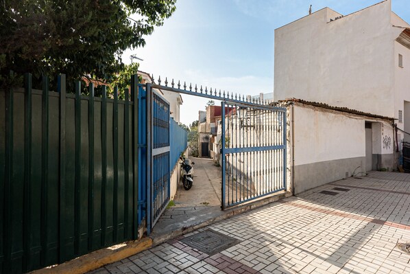 A gated entrance with a scooter parked inside, a paved pathway, and a building with a white facade.