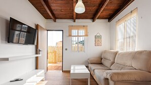 A modern living room with a sofa, a coffee table, a TV mounted on the wall, and a wooden ceiling.