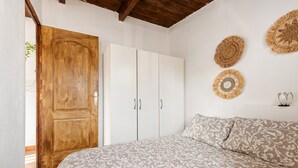 A bedroom with a wooden door, white wardrobe, patterned bedspread, and woven wall hangings.