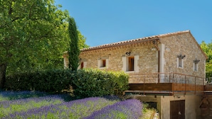 Un edificio de piedra con balcón, rodeado de campos de lavanda y vegetación.