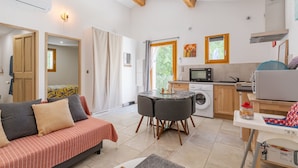 Un espacio habitable compacto con sofá, una mesa de comedor con sillas, una zona de cocina con lavadora y un televisor.