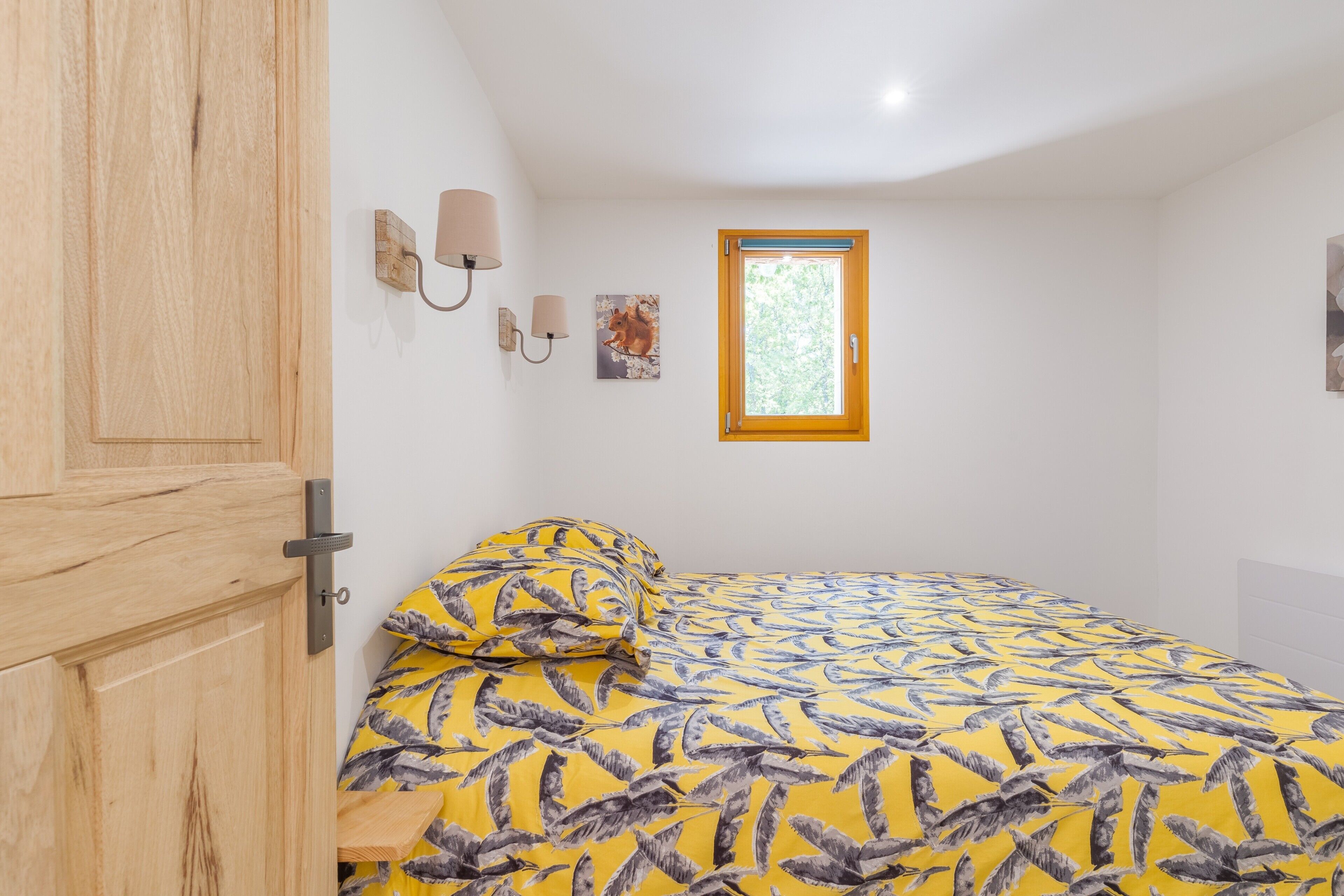 Une chambre à coucher comprenant un lit, une armoire en bois, une fenêtre et des lampes fixées au mur.