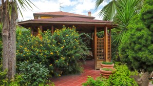 A covered outdoor area with a tiled floor, surrounded by lush greenery and flowering plants. - Cozy apartment in Trecastagni with swimming pool (Trecastagni)