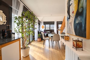 A modern kitchen with a dining area, large windows, and a staircase leading to another level.