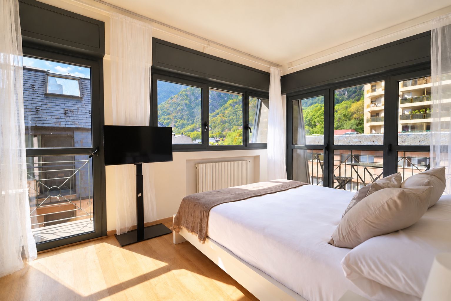 A bedroom with a bed, a TV, a window, and a balcony.