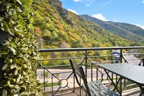 A balcony with a metal railing, a table, and a chair, overlooking a mountainous landscape.