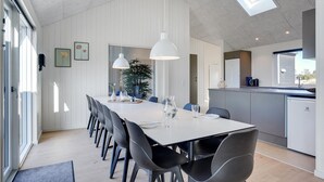 A modern kitchen with a central island, a dining area with a long table and chairs, and a view of the outdoors through a skylight. - Lovely home in Vejers Strand with sauna (Vejers Strand)