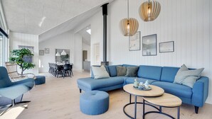 A spacious living room with a blue sectional sofa, a round coffee table, and a dining area with a white table and chairs. - Lovely home in Vejers Strand with sauna (Vejers Strand)