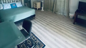 A hotel room with a bed, a desk, a chair, a TV, a ceiling fan, and a window with curtains. - Guest Suite East Boca! Near Beach & Restaurants! Near FAU! Close to I-95! (Boca Raton)