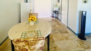 A dining area with a table set for two, a patterned tablecloth, and a vase with sunflowers. There is a microwave and a small shelf in the background. - Guest Suite East Boca! Near Beach & Restaurants! Near FAU! Close to I-95! (Boca Raton)