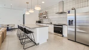 Een moderne keuken met een centraal eiland, barstoelen, roestvrijstalen apparatuur en hanglampen.