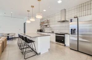A modern kitchen with a central island, bar stools, stainless steel appliances, and pendant lighting. - New 2B2B near Stanley Marketplace (Aurora)