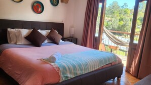 Un dormitorio con una cama grande, cabecero, mesita de noche, ventana con cortinas y vistas a zonas verdes.