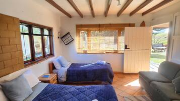 Quarto com duas camas, um sofá, uma janela com persianas e vista para o exterior.