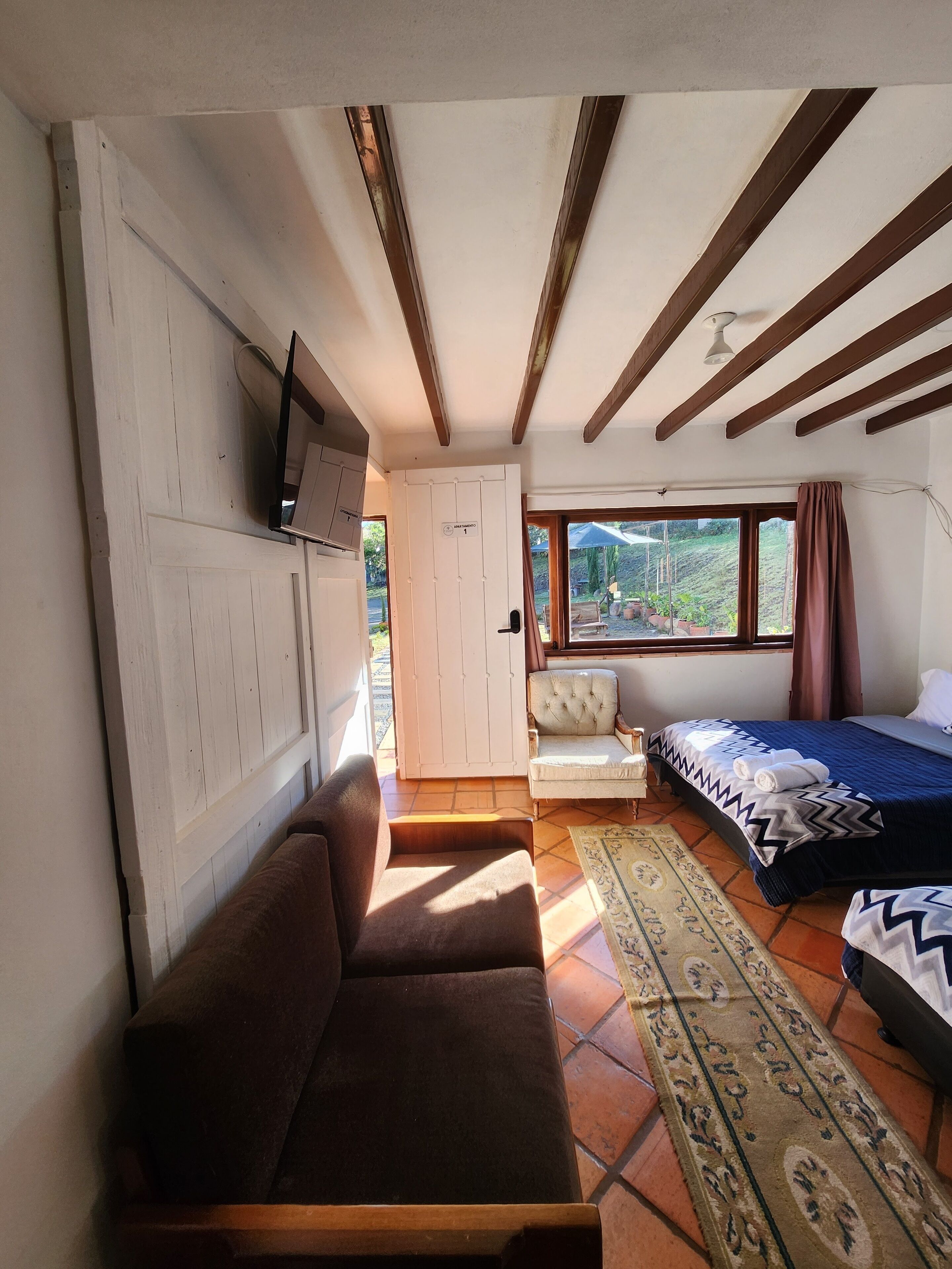 Una habitación compacta con sofá, cama, una mesita y televisor instalado en la pared.