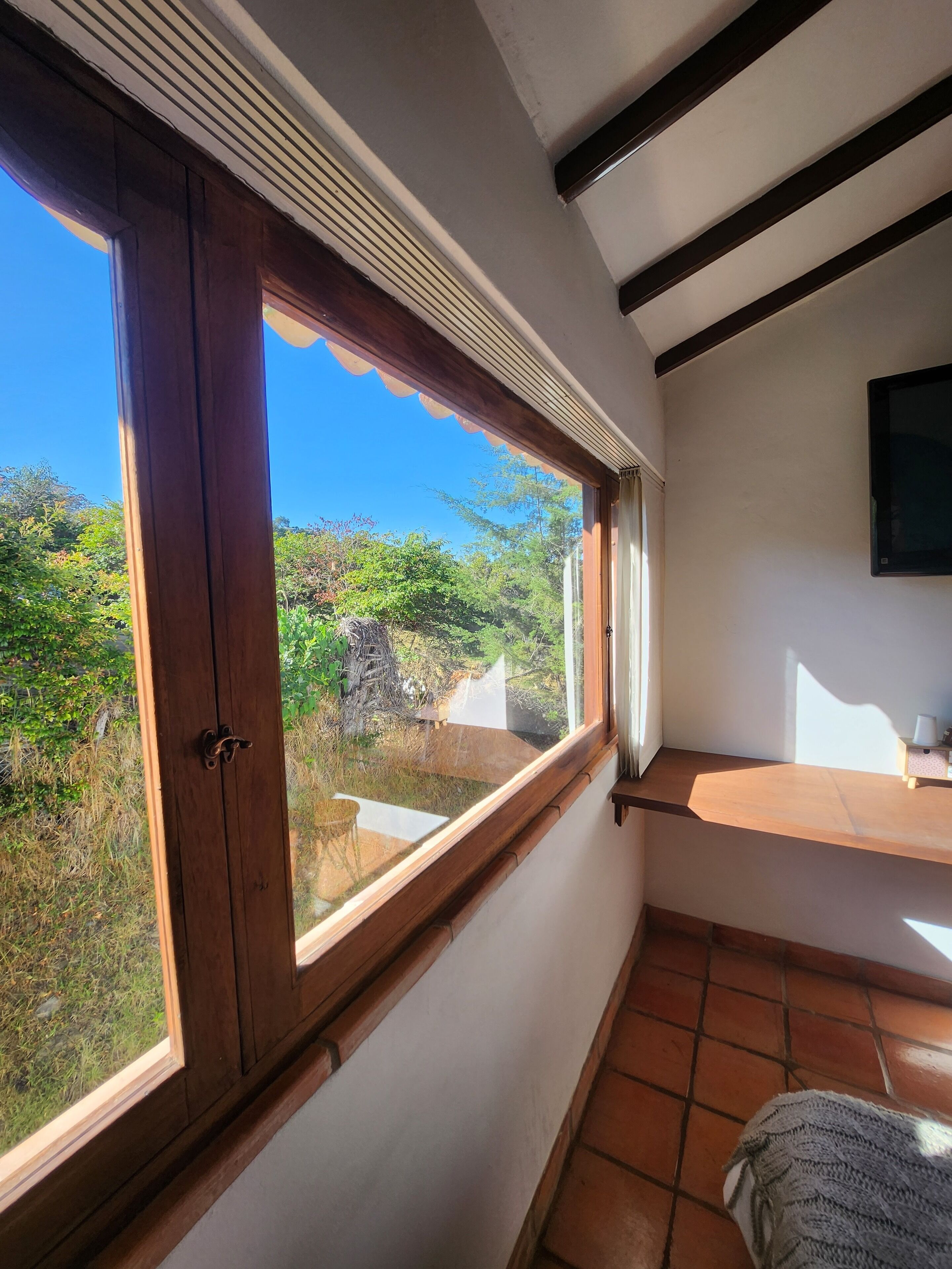 Una habitación con un ventanal grande, techo de madera y suelo de baldosas.