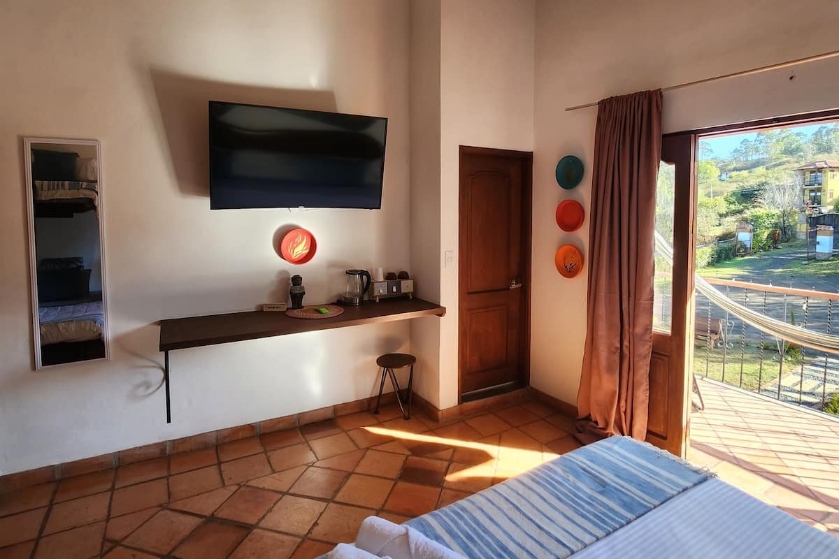 A bedroom with a bed, a TV, a small table with a kettle, and a door leading to a balcony.