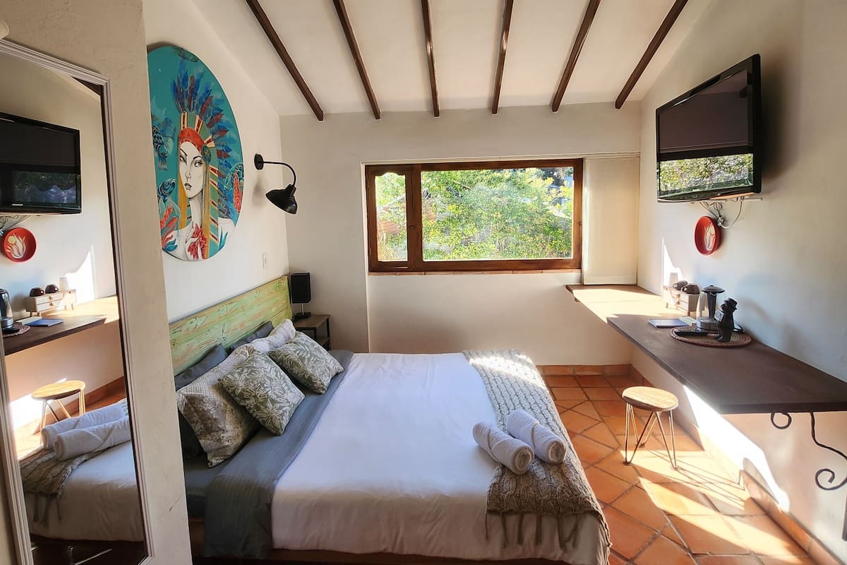 A bedroom with a bed, a desk, a TV, and a window.