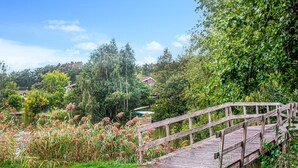 A wooden bridge leading to a dock over a body of water, surrounded by lush greenery and trees.